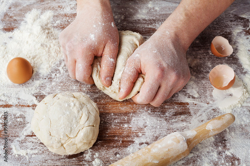 Baker prepares the dough on a wooden table, male hands knead the dough with flour, homemade dough for bread or pizza, top view, rustic style