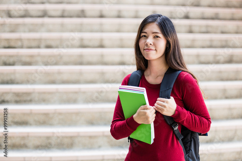 Smiling college student sitting on staircase and studying with b