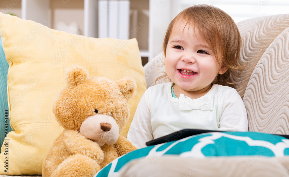 Happy toddler girl with her teddy bear and tablet pc