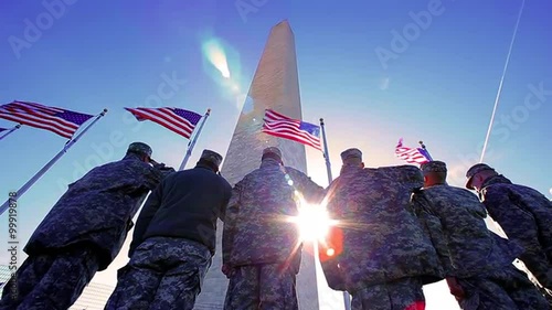 American soldiers saluting the American Flag at the Washington monument with blue sky and lens flare, patriotic.  Handheld.