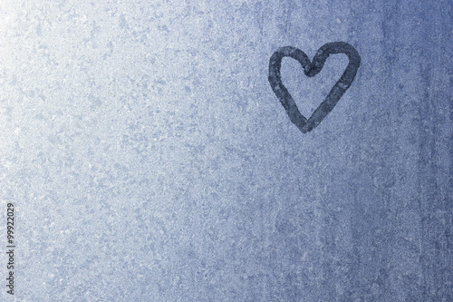 Heart on frozen glass. Ice on a window background. Small blue