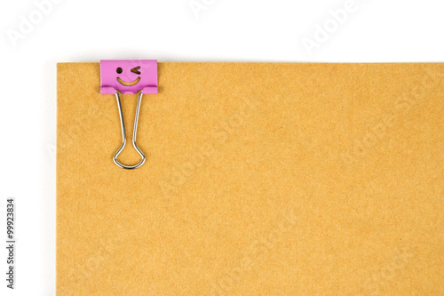 Pink happy face paperclip nipped at brown paper on white background. 