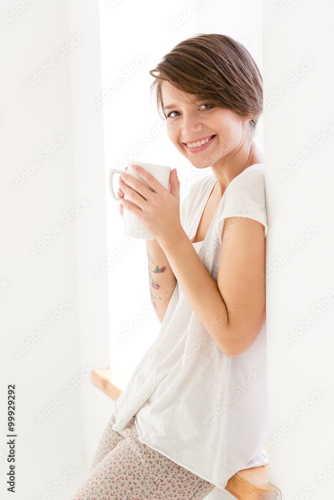 Cute cheerful young woman in pajamas drinking tea Cute cheerful young woman in pajamas drinking tea