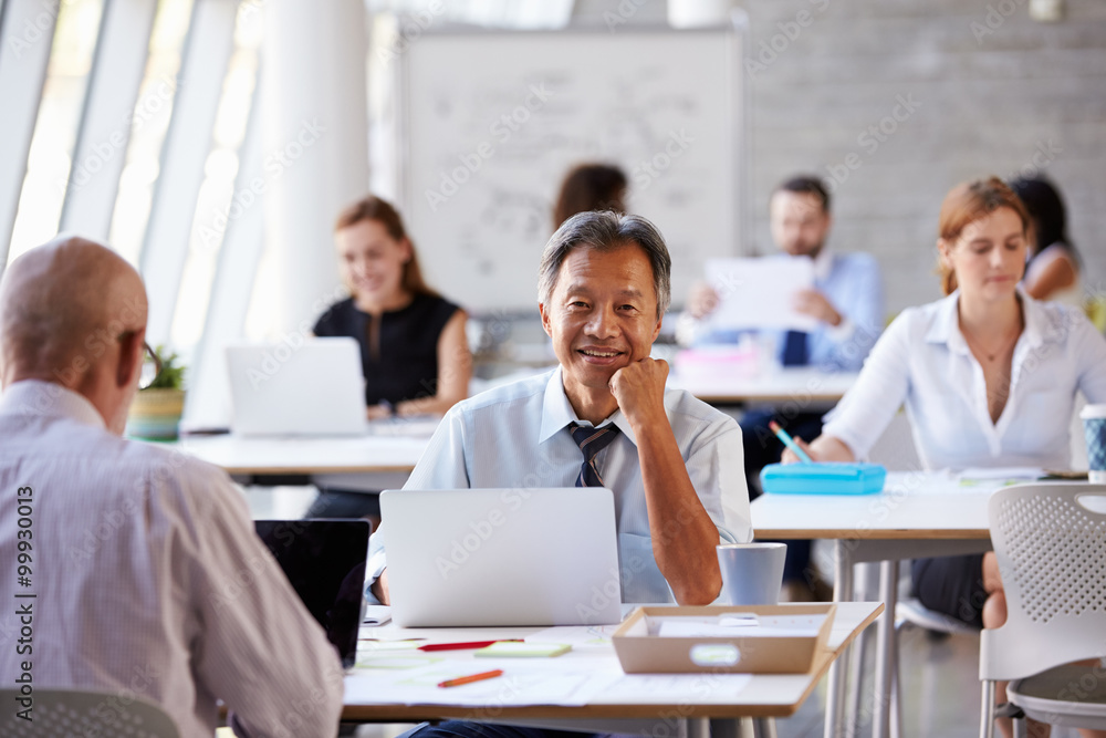 Portrait Of Businessman Working On Laptop In Busy Office