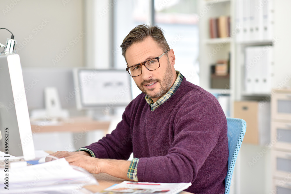 Smiling businessman with eyeglasses sitting in office Smiling businessman with eyeglasses sitting in office