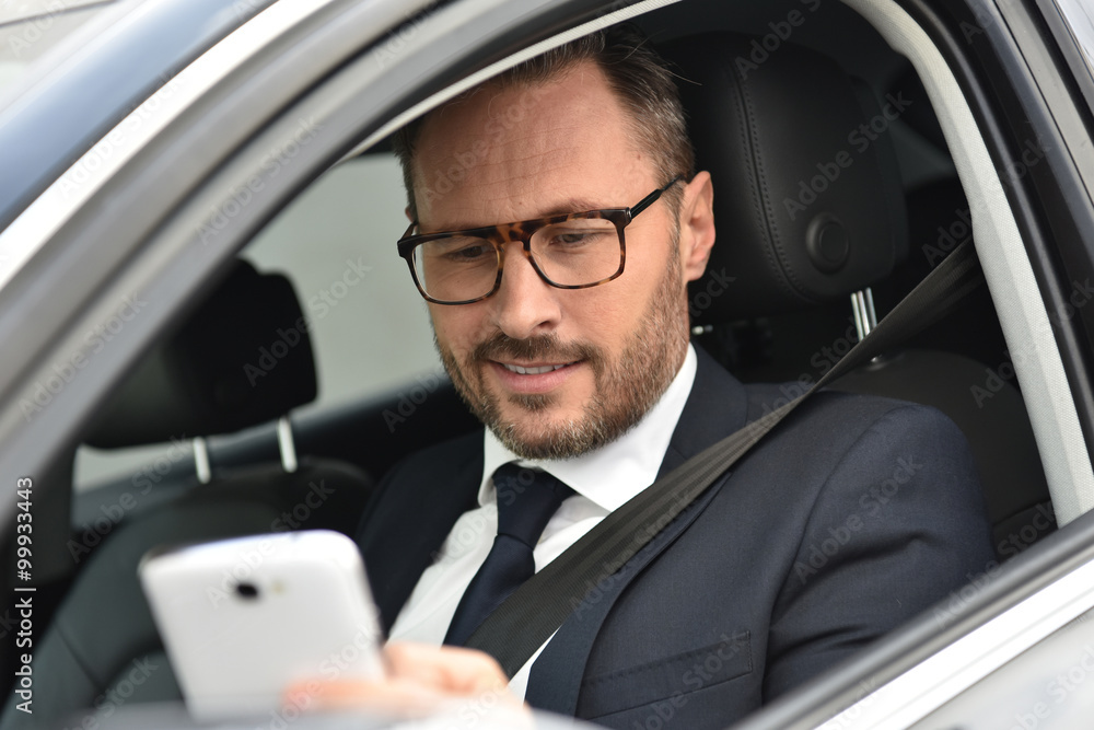 Businessman in car reading message on smartphone