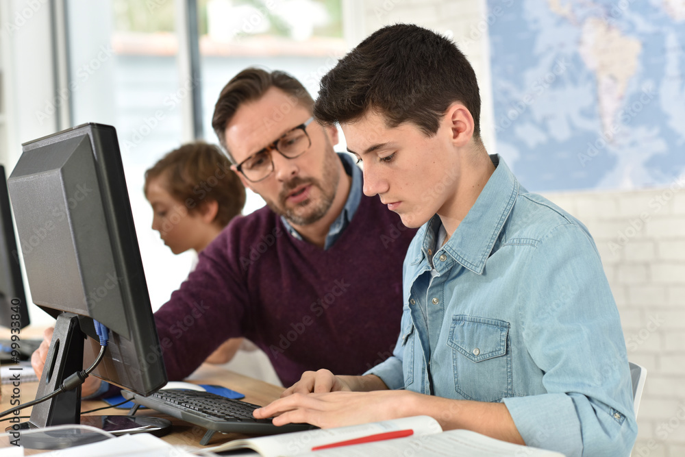 Teacher in computing class assisting teenager with tablet Teacher in computing class assisting teenager with tablet