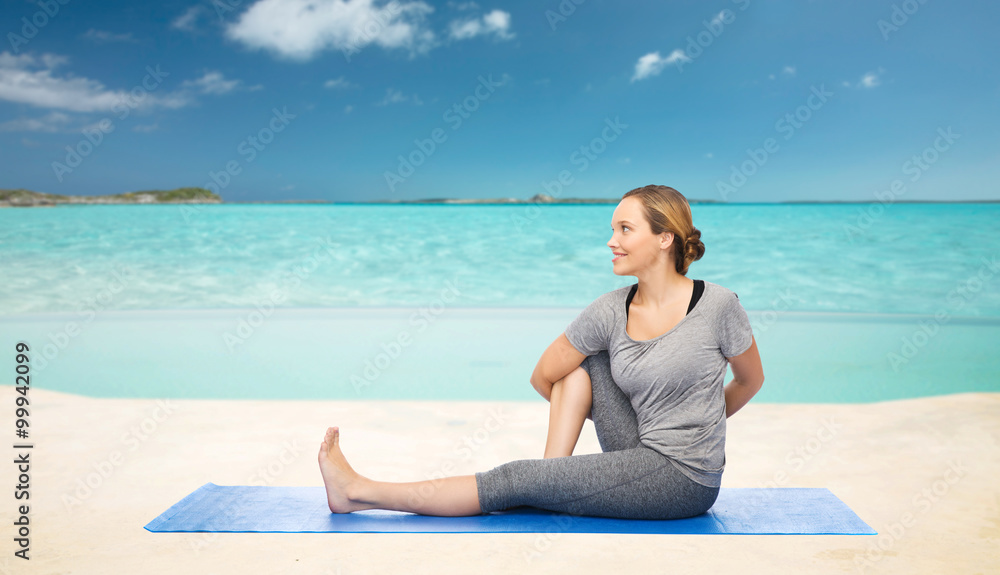 Fototapeta premium woman making yoga in twist pose on mat over beach 