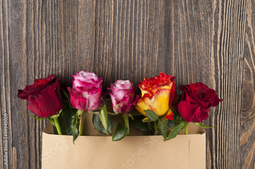 Bunch of multicolor rose flowers in paper envelope over wooden b