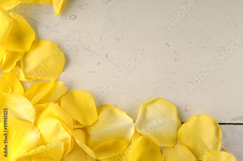 Frame of yellow rose petals on a wood background.