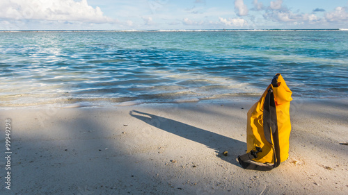 Light and shadow on sandy beach with yellow waterproof bag