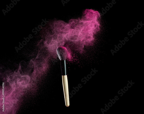 Make-up brush with pink powder explosion on black background