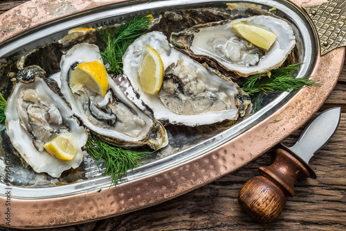 Obraz na plátně Opened oysters with piece of lemon on the cooper tray.
