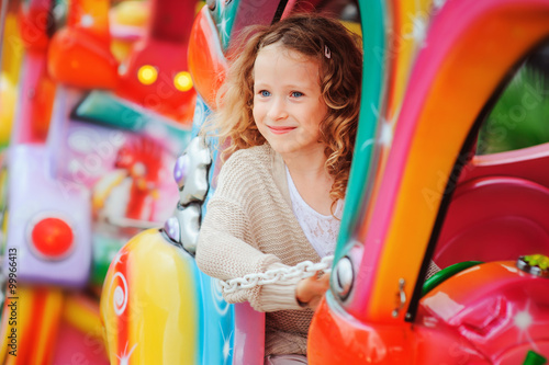 Photography happy child girl riding train on funfair on summer vacation