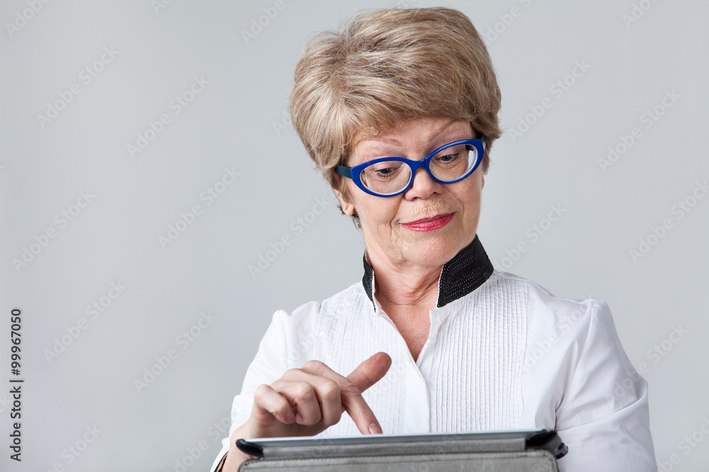 Senior woman with a smirk pushing the button at the tablet screen, portrait on a gray background Senior woman with a smirk pushing the button at the tablet screen, portrait on a gray background