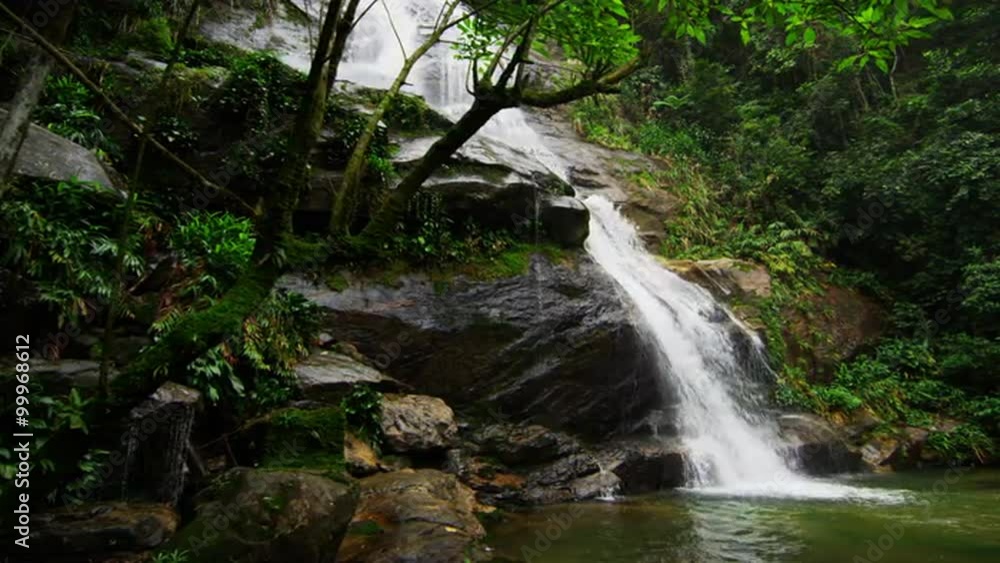 Tracking shot of a jungle waterfall cascading into a deep green pool. Tracking shot of a jungle waterfall cascading into a deep green pool.
