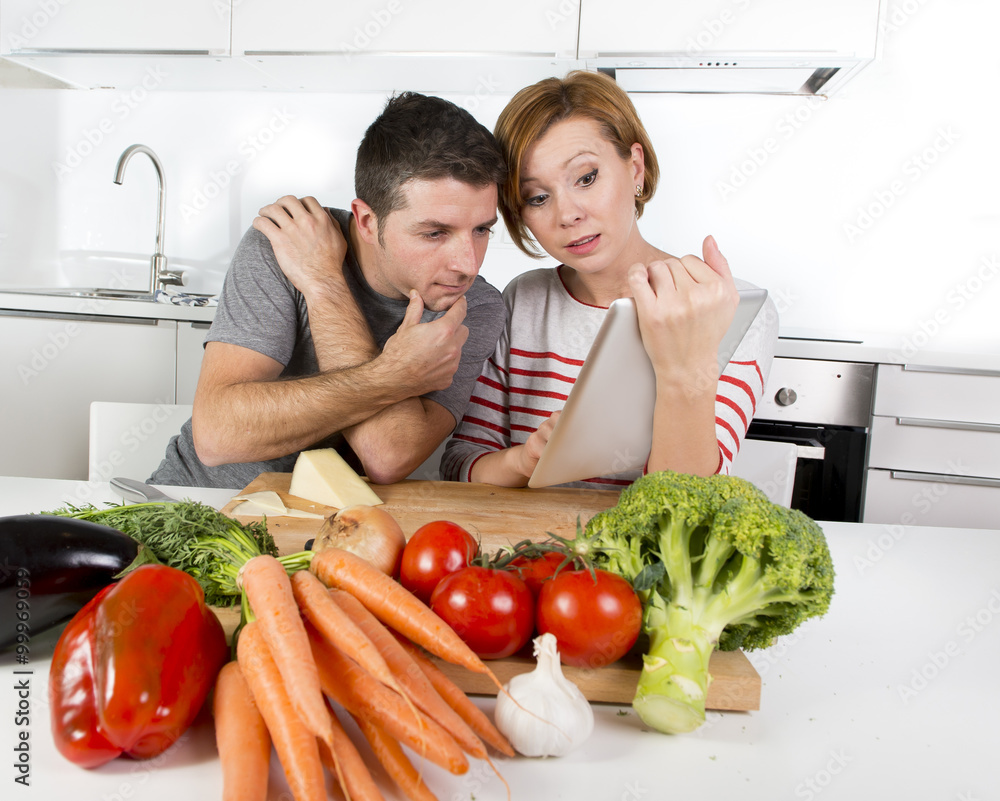 American couple in domestic kitchen wife following recipe in digital pad working together with husband American couple in domestic kitchen wife following recipe in digital pad working together with husband