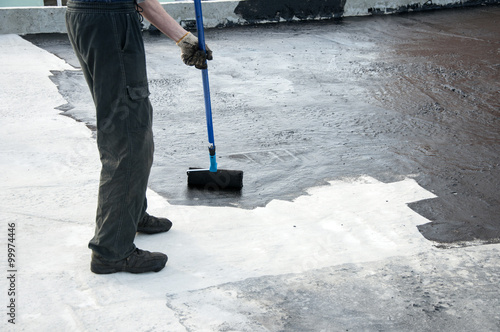 Roofer worker painting  bitumen praimer at concrete surface . Waterproofing. Waterproof roof. photo
