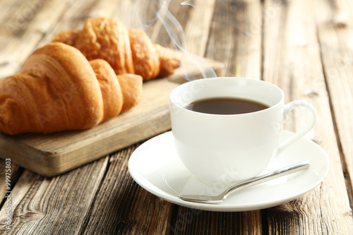 Tasty croissants with cup of coffee on brown wooden background