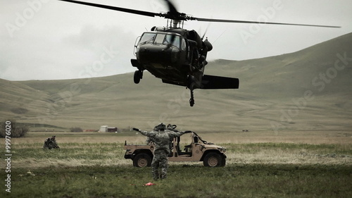 Shot from ground of Black Hawk helicopter hovering above Humvee while soldier gives signals to pilot. photo