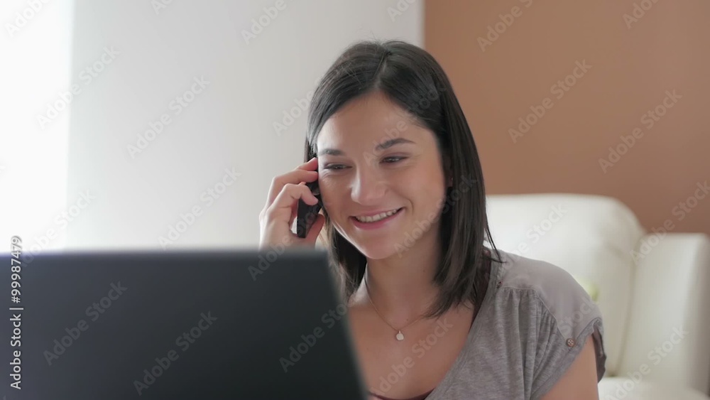 Slow motion of a nice girl browsing laptop and talking over phone at home close up Slow motion of a nice girl browsing laptop and talking over phone at home close up
