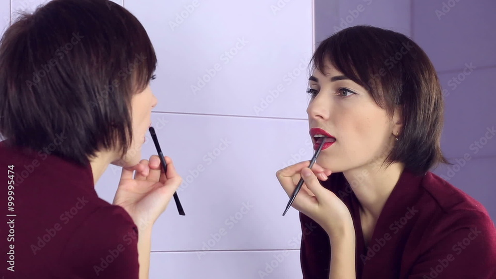 Beauty woman applying makeup. Beautiful girl looking in the mirror and paints her lips with brush. Beauty woman applying makeup. Beautiful girl looking in the mirror and paints her lips with brush.