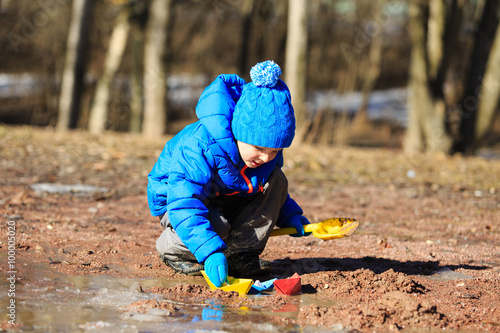 little boy plaing with paper boats in spring puddle