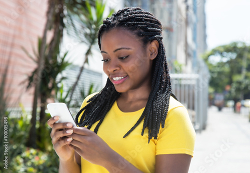 Lachende Afrikanerin im gelben Shirt surft mit dem Handy photo