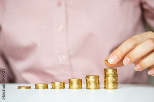 Female hand stacking gold coins into increasing columns