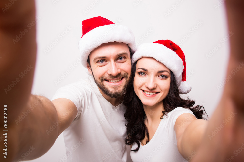 christmas, holidays, technology and people concept - happy couple in santa hats taking selfie picture with smartphone on white background christmas, holidays, technology and people concept - happy couple in santa hats taking selfie picture with smartphone on white background