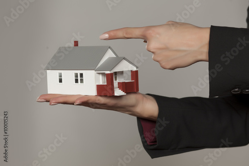 female hands holding a model house and pointing