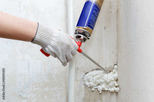 Worker's hand fix a rent in wall using polyurethane foam photo