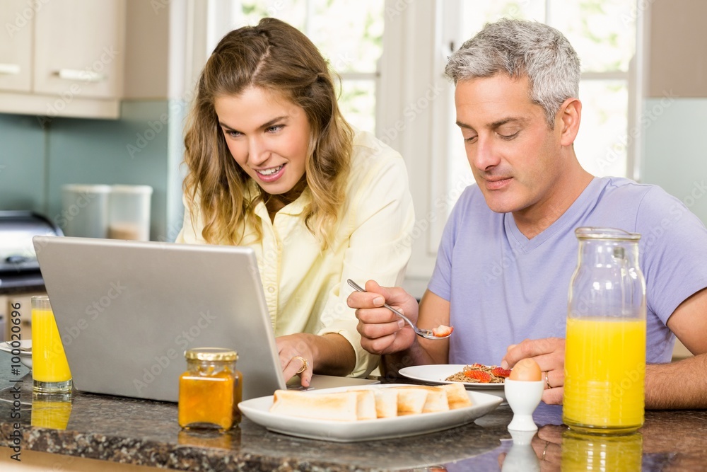 Happy couple using laptop and having breakfast Happy couple using laptop and having breakfast