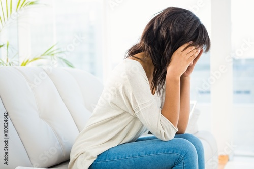 Woman holding her head while sitting on the couch