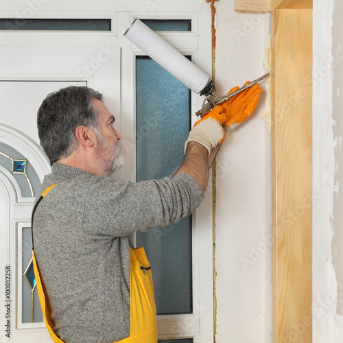 Worker installing wooden door, using polyurethane foam