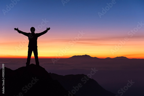 silhouette of man standing and spread hand on the top of mountai