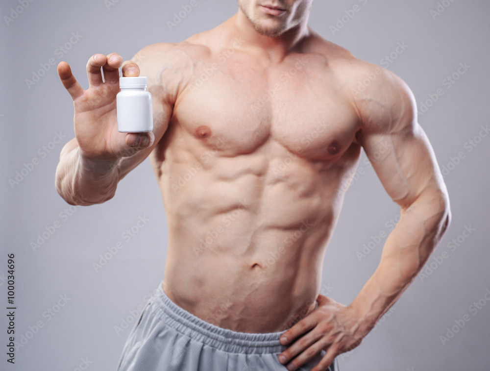 Bodybuilder with a white jar of pills on neitral background. Studio shot Bodybuilder with a white jar of pills on neitral background. Studio shot