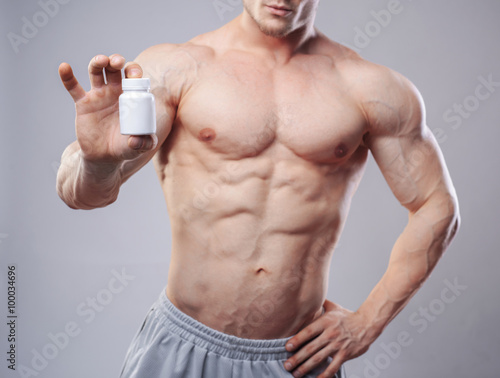 Bodybuilder with a white jar of pills on neitral background. Studio shot