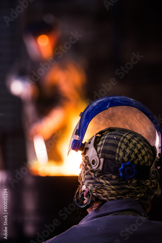 Steel worker in protective clothing raking furnace in an industr