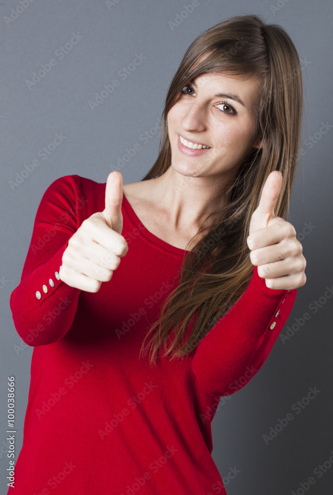 optimism concept - discreet beautiful young woman smiling with thumbs up in the foreground for dynamic victory, studio grey background optimism concept - discreet beautiful young woman smiling with thumbs up in the foreground for dynamic victory, studio grey background