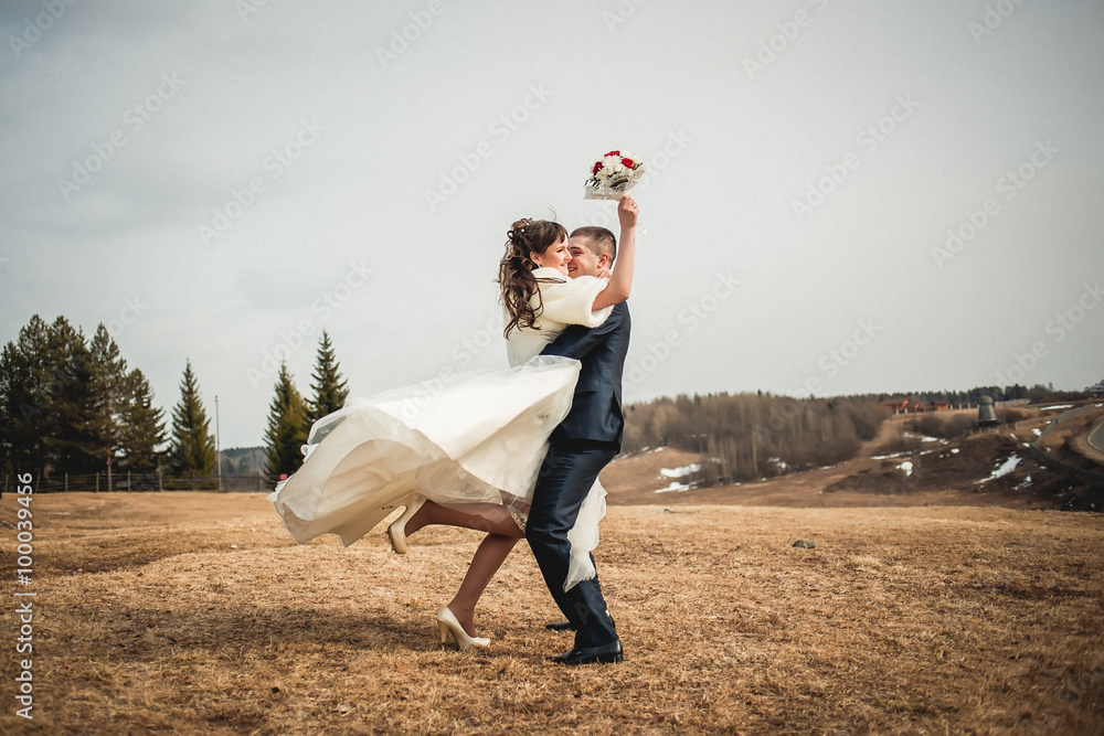Wedding  couple embracing on open spaces at winter The groom lifts the happy bride with bouquet