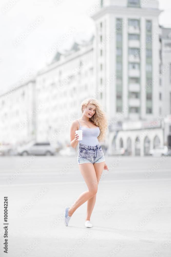 Happy smile / Happy young woman with long curly hair, holding a take away coffee cup and smiling with flirt in front of a camera against urban city traffic background. Happy smile / Happy young woman with long curly hair, holding a take away coffee cup and smiling with flirt in front of a camera against urban city traffic background.