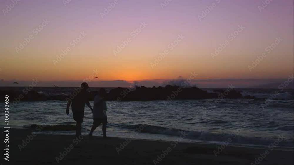 Slow motion static view of 2 people walking on the beach at sunset. Slow motion static view of 2 people walking on the beach at sunset.