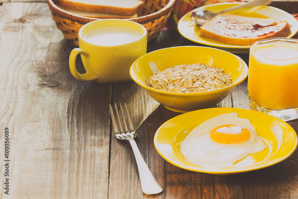 Breakfast served in yellow tableware - eggs, oatmeal, orange juice, milk, on wooden background