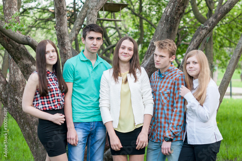 Five young friends happy graduates posing in the summer park