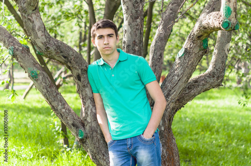 a young man in a green T-shirt posing in park near tree