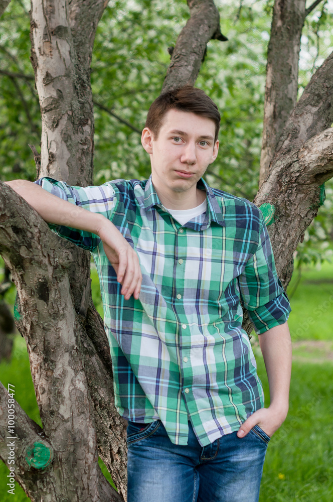 a young man in a plaid green shirt posing in a park in spring a young man in a plaid green shirt posing in a park in spring
