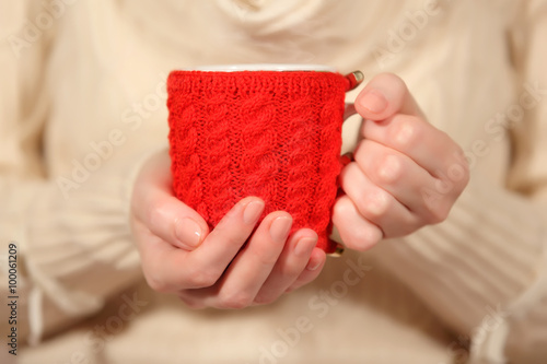 A woman holding a cup of hot drink, on which have handmade knitted cover