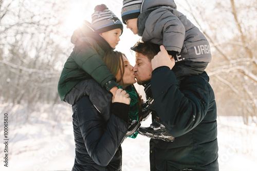 Cute young family with twins and pregnant young mother having fun in winter park on a bright day hugging each other and smiling
