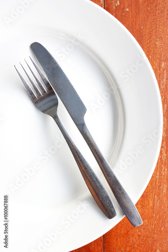Fork and knife in white plate on wooden table.